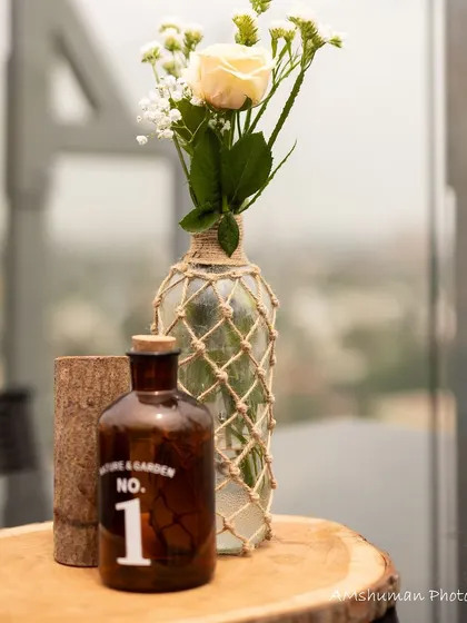 A close-up of a decor detail from a boho baby shower. A rustic bottle and a macrame-wrapped vase with a single white rose create a simple yet beautiful and thematic accent.
