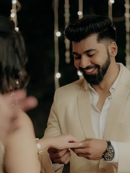 The groom's happy expression as he places the ring on his bride-to-be's finger, seen from her perspective.