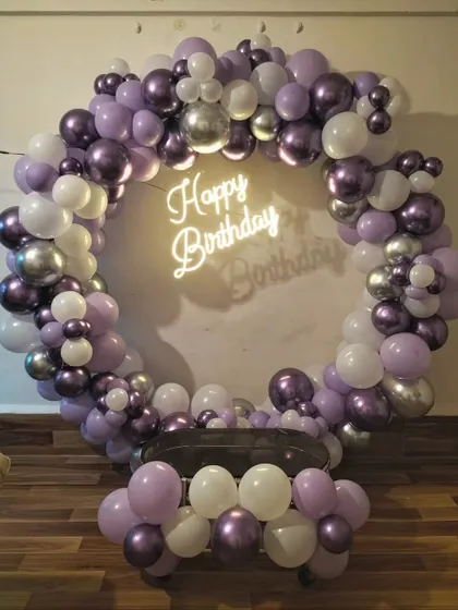 A simple and elegant balloon ring in shades of purple and white with a neon sign, perfect for a cake-cutting ceremony at home.