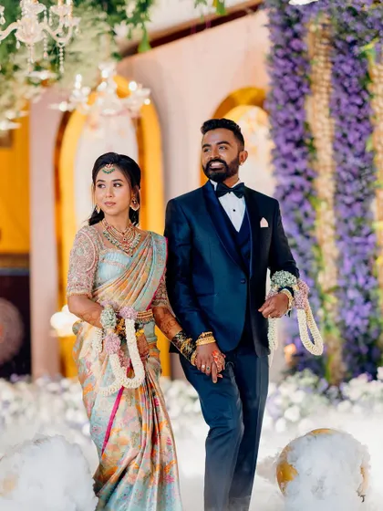 The groom looks dapper in a dark navy tuxedo with a bow tie, a classic choice for a formal wedding reception. It provides a sharp, modern contrast to the bride's traditional saree.