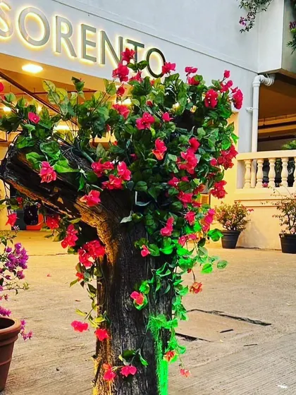 An artificial flowering tree installed outside a hotel entrance. The bright red flowers are wrapped around a real tree trunk for a realistic and eye-catching display.
