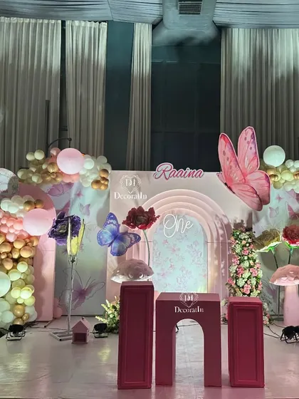 A full view of the whimsical stage for the butterfly-themed party, complete with a cake-cutting pedestal set, a custom arched backdrop, and enchanting props.