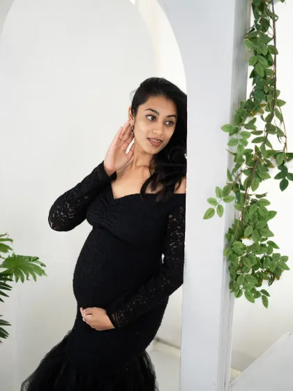 A candid and elegant portrait of a mom-to-be in a black lace gown, peeking out from behind a white archway in our studio.