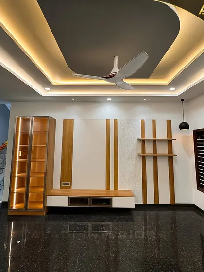 A spacious living area with a dark marble floor and a striking false ceiling with curved cove lighting. The room features a modern TV unit and a glass-front display cabinet.
