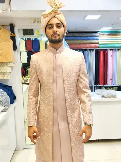This heavy-embroidered open sherwani in a soft peach tone offers a modern silhouette for the groom. It's layered over a matching kurta for a sophisticated, layered appearance.
