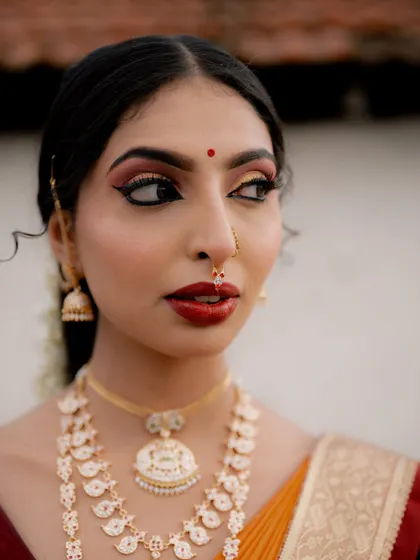 A detailed close-up focusing on the bride's striking makeup. The winged eyeliner and bold red lip are hallmarks of a classic Indian bridal look.