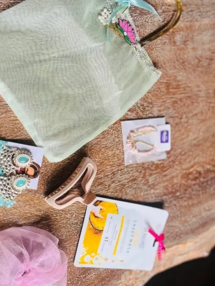 A flat-lay of items for a sister's Rakhi gift, including earrings, a hair clip, a face mask, and a scrunchie.