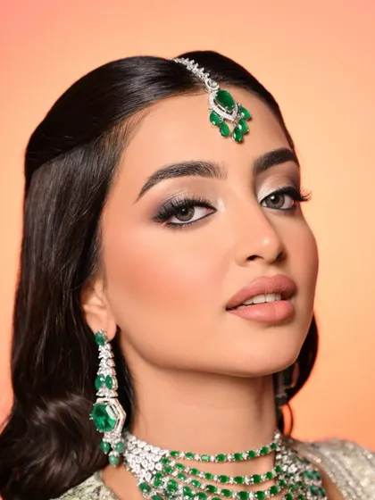 A detailed portrait that highlights the flawless base, subtle contouring, and the way the emerald green of the jewellery makes the entire look pop.