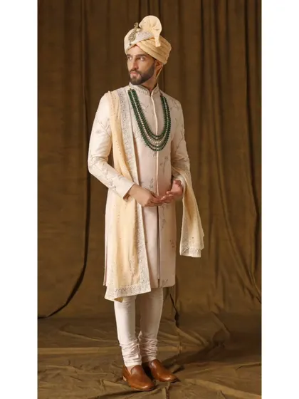 The Jashn-e-Ada sherwani in a soft blush peach. The handwoven fabric is adorned with captivating threadwork and a touch of gold, embodying contemporary regal charm.