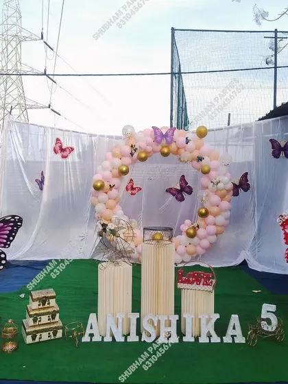 An outdoor butterfly-themed 5th birthday party with a circular balloon arch and props.