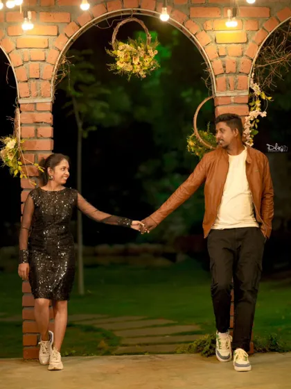 A romantic night shot with the couple holding hands under brick arches. The warm lighting creates a cozy and intimate atmosphere.