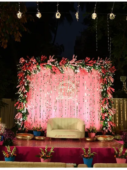 A stage that glows with glamour. The shimmering pink sequin backdrop, framed with lush flowers, creates a vibrant and celebratory atmosphere perfect for a sangeet or reception night.