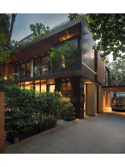 The 'Regeneration of a 70's Suburban Build' by A L V A architects, a WAF Retrofit shortlist. This exterior view shows the transformed Mumbai home at night, with its modern metallic facade, integrated lighting, and lush greenery.