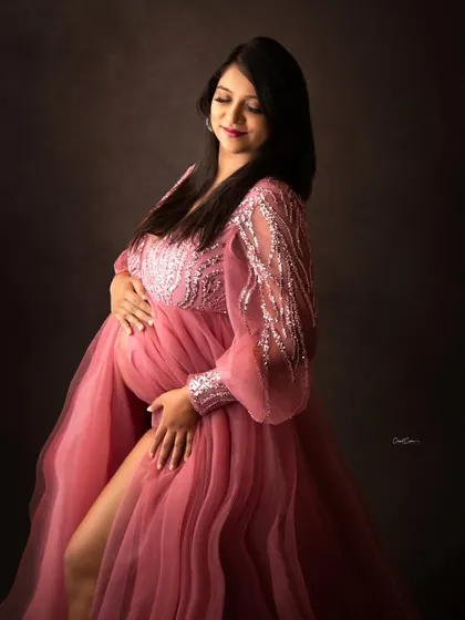 A serene and beautiful portrait. The mom-to-be cradles her bump in a dusty pink gown with sparkling, sheer sleeves.