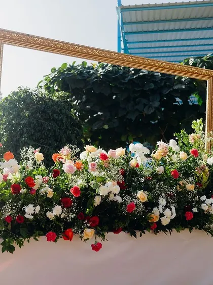 A photo booth with a large golden frame and a base of colorful flowers.