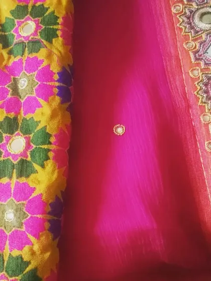 This image shows a combination of fabrics for a festive outfit. On the left is a colorful phulkari-style embroidered fabric with mirror work, paired with a sheer pink georgette that has a detailed embroidered border.