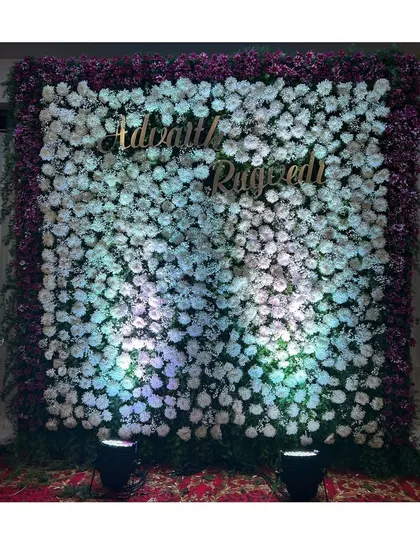 An elegant floral backdrop for a naming ceremony. The wall is densely packed with white and purple flowers, with the baby's name in a golden script at the center.
