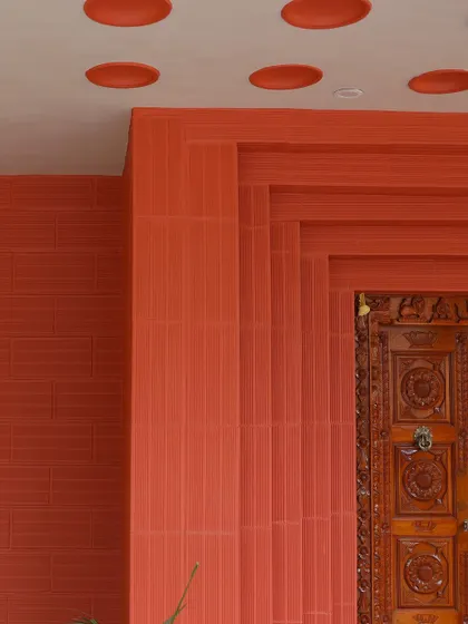 A detail shot of the facade, showing the texture of the red brickwork, the layered door frame, and the unique circular cutouts in the ceiling.