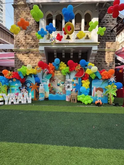 A vibrant and colorful pool party backdrop with balloons, fruit cutouts, and a lit-up name.