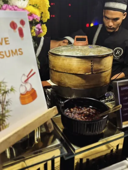 A close-up of our live dim sum station, featuring a menu with options like Singhai Veg and Chicken Hot Basil. The traditional bamboo steamers and illustrated sign add to the authentic Pan-Asian theme.