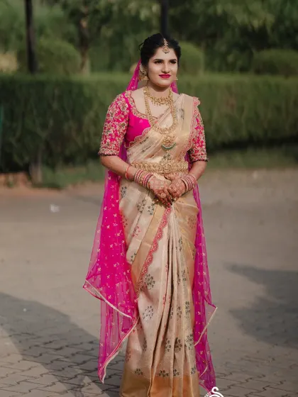 A full-length view of the bride in her cream and pink saree, with a sheer pink veil adding a touch of modern elegance.