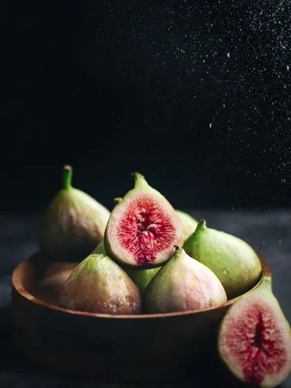 A dark and moody still-life of fresh figs, with a spritz of water captured mid-air to enhance their freshness and add drama.