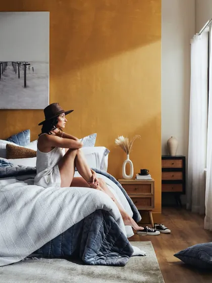 A lifestyle shot for a bed linen brand, capturing a moment of quiet contemplation. The warm, natural light and thoughtful styling create an authentic and aspirational bedroom scene.