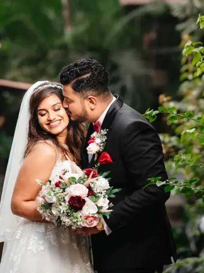 A sweet and tender moment between the newlyweds. The groom's gentle kiss on his bride's cheek is a simple gesture filled with love and affection, captured in soft, natural light.