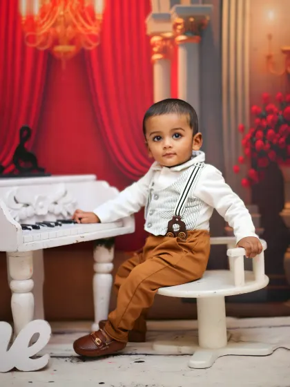 A dapper little musician poses at a miniature white piano for his first birthday portraits.