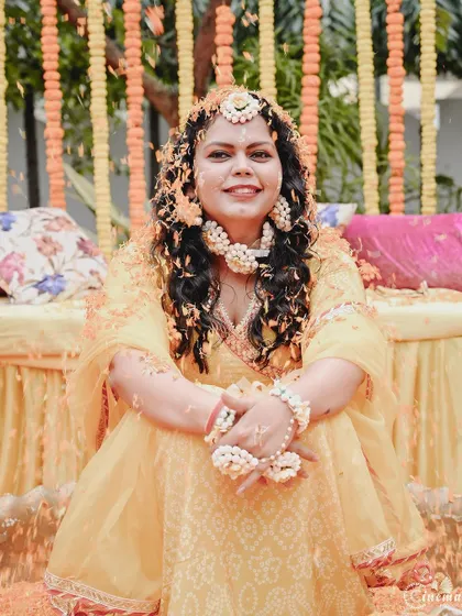 A smiling portrait of the bride after the rituals, covered in haldi and flower petals.