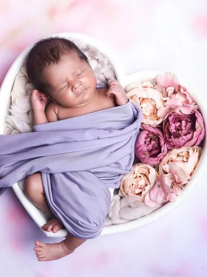 A beautiful pose with a baby partially wrapped in a lavender cloth, sleeping in a heart-shaped bowl filled with flowers.