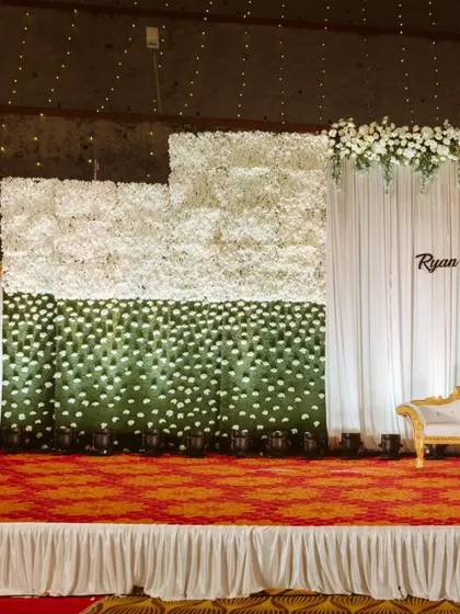 A unique stage backdrop featuring a wall of white and green florals, creating a modern and refreshing look for Ryan and Ela's reception. The clean lines and simple color palette exude elegance.
