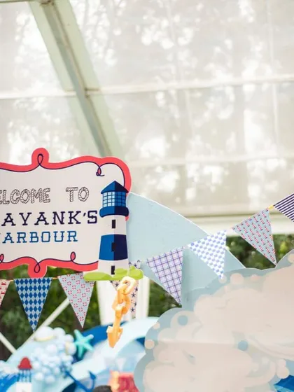 A welcome sign for "Prayank's Harbour," a nautical-themed party. The sign is decorated with a lighthouse and lifebuoy, and surrounded by festive bunting, setting the stage for a seaside adventure.