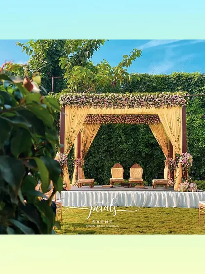 A view of the colorful contemporary mandap from a distance. The lush green lawn and clear blue sky provide the perfect backdrop for this joyful and love-filled celebration.