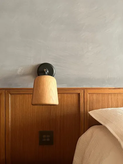 A wall-mounted bedside lamp is perfectly integrated with the wooden dado and limewashed wall. The simplicity of the fixture complements the rich textures of the wall treatments.