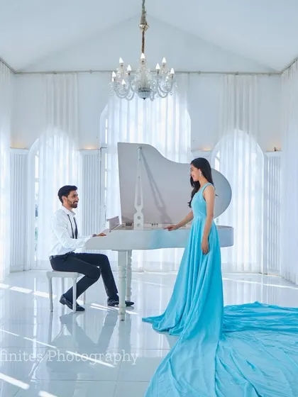Our all-white studio, complete with a grand piano, provides a backdrop for timeless elegance. The flowing trail of this light blue gown adds a touch of drama and sophistication to this classic couple portrait.