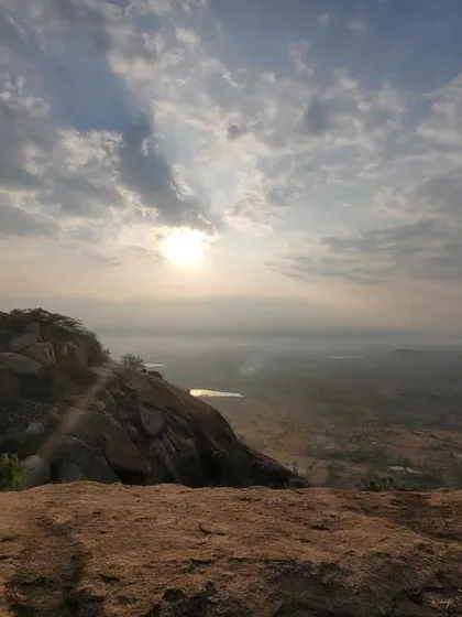 The sun breaking through the clouds, casting a golden light over the vast plains visible from the top of the hill.