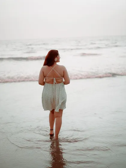 The bride walking into the gentle waves. This thoughtful, serene portrait captures a moment of peace and reflection during her beach photoshoot.