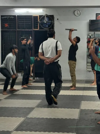 A look at our group strength training from behind. Students are engaged in various exercises, including overhead presses with bars, demonstrating the diversity of our workout programming.