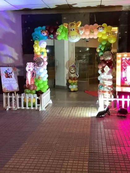 An outdoor entrance arch for a jungle-themed party, featuring a giraffe foil balloon and a personalized light-up sign.