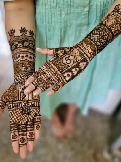 A stylish engagement mehendi with a peacock on one palm and interlocking rings on the other. The design is modern, with a lotus armlet and geometric patterns.