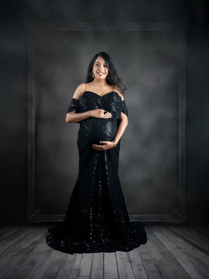A solo portrait is a powerful way to celebrate you and your bump. This shot from a studio session features one of our popular black sequin gowns against a moody, dramatic backdrop, highlighting the mother's radiant glow.