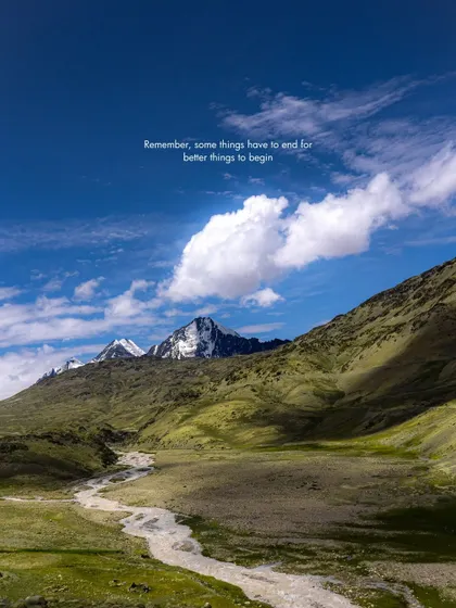 A beautiful summer day in the Himalayas. The lush green valley, winding river, and snow-capped peaks under a blue sky create a perfect, picturesque scene.