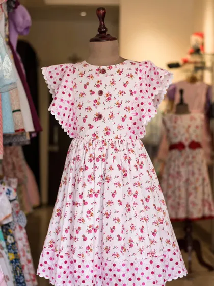 A sweet and playful dress combining a pink floral print with pink polka dots. The flutter sleeves with scalloped edges add a charming, whimsical touch.