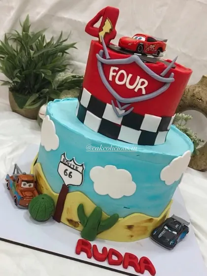 A two-tier Disney Cars themed cake for a 4th birthday. This fun design features a desert road scene on the bottom tier and a racetrack on top, complete with Lightning McQueen and other characters.