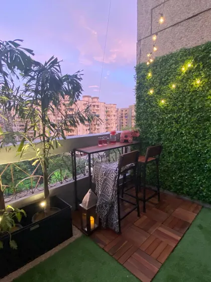 We created this charming bar nook on a small balcony using interlocking wood deck tiles and a patch of artificial grass. The setup is perfect for enjoying the evening, with a vertical garden and string lights adding to the warm, inviting atmosphere.