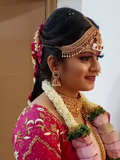 A side profile showing the details of the bridal updo and makeup. The hairstyle is secured neatly to hold the weight of the headpiece and veil, while the makeup highlights her features beautifully.