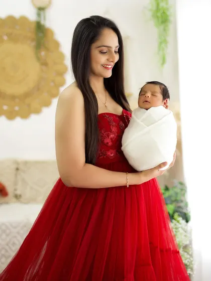 A mother in a beautiful red dress, smiling as she holds her sleeping newborn. The image is full of warmth and maternal love.
