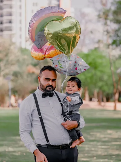 A father holds his son and a bunch of festive balloons. This portrait combines a posed moment with the fun and color of props.