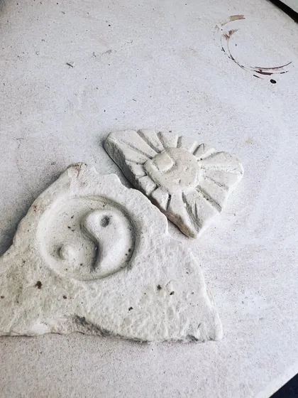 Small carved pieces showing a yin-yang symbol and a sun, made by participants experimenting with different designs.
